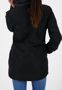 Czarna zewnętrzna kurtka o gładkiej fakturze, z taliowanym krojem i logo jako ozdobą. Połączona z niebieskimi dżinsami.