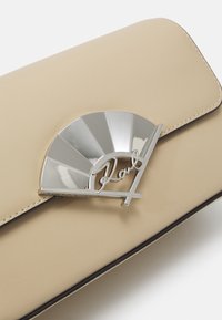 Clutch in pelle beige con una chiusura a ventaglio color argento che presenta un logo. Texture liscia e bordo nero a contrasto lungo i bordi.