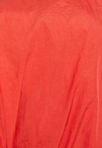 Texturerad tyg i en livlig korallfärg, med subtila veck och ett draperat utseende, som framhäver mjukhet och lätthet.