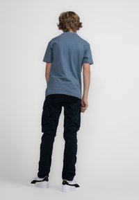 Blauwe katoenen t-shirt met korte mouwen, gecombineerd met zwarte cargobroeken. Schoenen zijn witte en zwarte sneakers. Eenvoudig en casual ontwerp.
