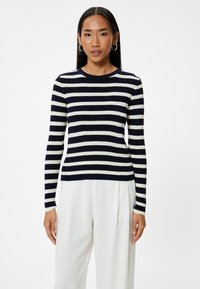 Marinblå och vit randig tröja med ribbad textur, rund halsringning och långa ärmar. Kombinerad med vita högmidjade byxor.