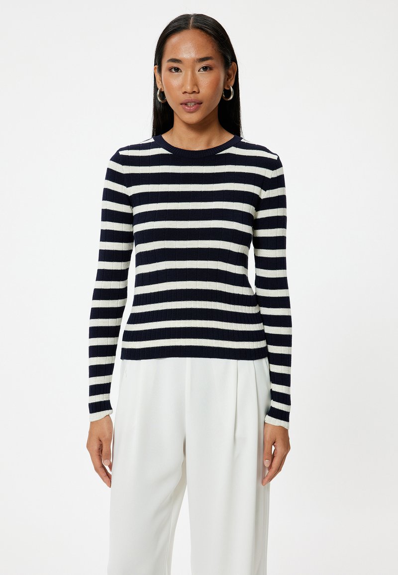 Marinblå och vit randig tröja med ribbad textur, rund halsringning och långa ärmar. Kombinerad med vita högmidjade byxor.