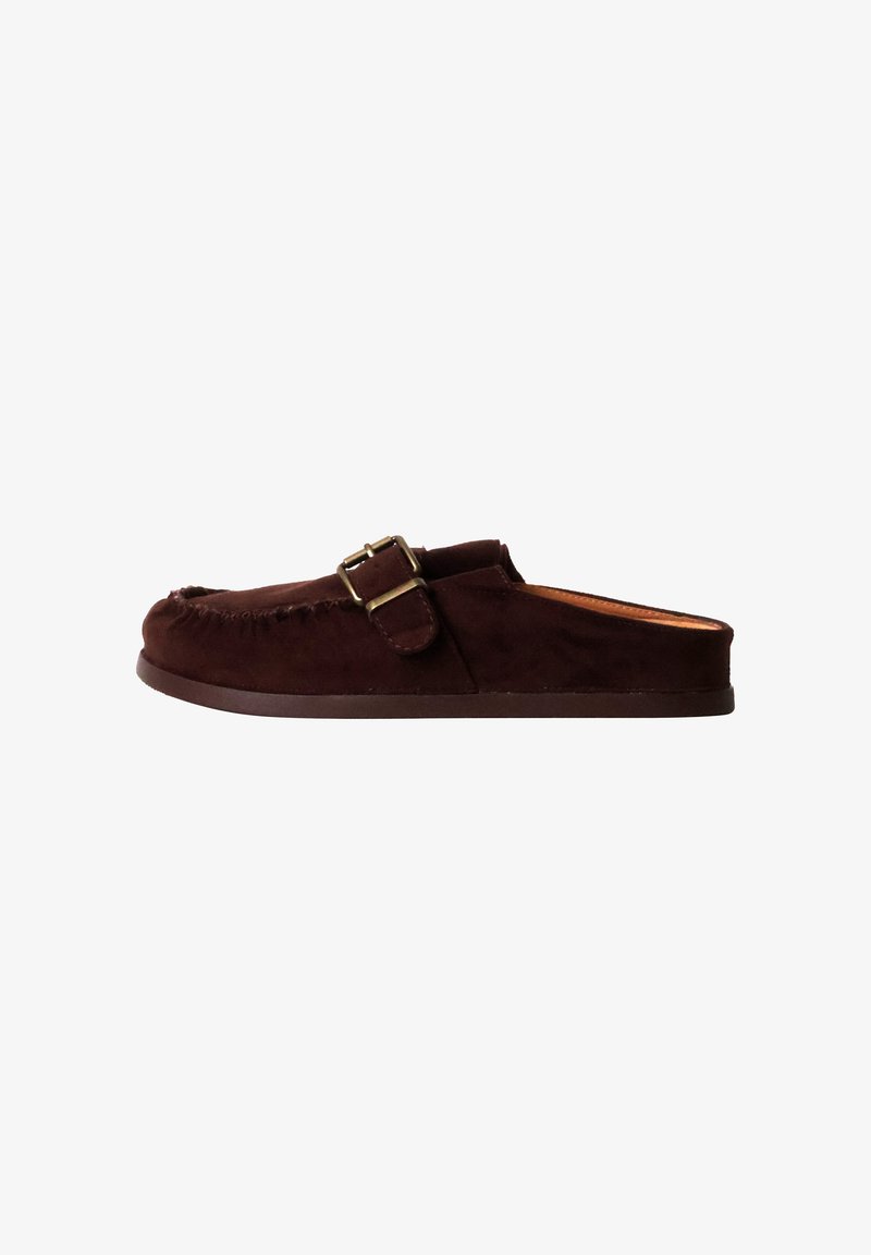 Mocassin en daim brun foncé à enfiler avec une boucle latérale et une semelle plate, vu de profil sur fond blanc.