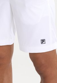 Witte shorts gemaakt van een lichtgewicht materiaal, met een zwart logo op de onderrand en een eenvoudig, strak ontwerp zonder patronen.