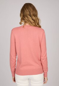 Pull en laine rose pâle, à enfiler, avec une texture douce, des manches longues et des côtes au niveau des poignets et de l'ourlet. Détails de couture visibles au niveau de l'encolure et du dos.