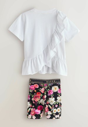 Balts īss krekls ar volānu diagonālu pārklājumu, kombinēts ar melniem ziedu raksta šortiem ar zīmola jostu.