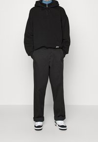 Felpa nera con cappuccio e zip, abbinata a pantaloni neri larghi e sneakers bianche con dettagli neri. Design minimale e vestibilità comoda.