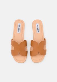 Brown leather slide sandals with a cross design, featuring a smooth texture, flat sole, and branding on the insole.