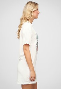 Biała bawełniana sukienka t-shirtowa z krótkimi rękawami, z kolorowym nadrukiem na przodzie oraz dopasowaną sylwetką. Gładka tekstura.