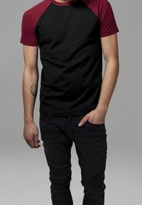 Černé tričko s burgundskými rukávy raglánového střihu, z bavlněného materiálu, přiléhavý design, krátké rukávy, v kombinaci s přiléhavými černými džínami s texturovanými detaily.