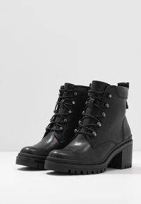 Mustat nahkaiset nilkkurit, joissa on kulutusta kestävä pohja, nauhakiinnitys, hopeanväriset metalliosat ja lohkokorko. Yläosassa teksturoitu pinta.