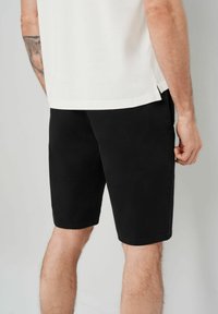 Czarne szorty wykonane z mieszanki bawełny z gładką fakturą, z bocznymi kieszeniami i czystym wykończeniem. Noszone z białą koszulą.