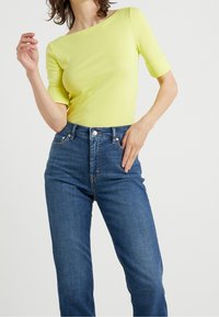 Gul figursydd topp med korta ärmar, båturringning, kombinerad med högmidjade blå jeans. Slät textur, minimala designelement.