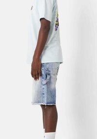 T-shirt azzurro chiaro a maniche corte con design grafico sulla schiena, abbinato a pantaloncini di jeans sbiaditi con orli sfrangiati e tasche laterali.