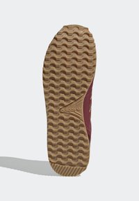 Podešev boty s hnědou vlnitou vzorovou drážkou a drsně upraveným podpatkem, se značkou Adidas vyraženou uprostřed, připevněná k bordeaux botě.