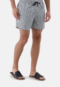 Navy- und weiße Blumen-Badehosen mit einem elastischen Bund und Kordelzug, kombiniert mit dunklen Sandalen mit einem geflochtenen Riemen-Design.