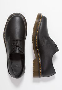 Chaussures en cuir noir avec une texture lisse, bout rond et semelle brune surélevée. Dotées de coutures jaunes et d'un design à lacets.
