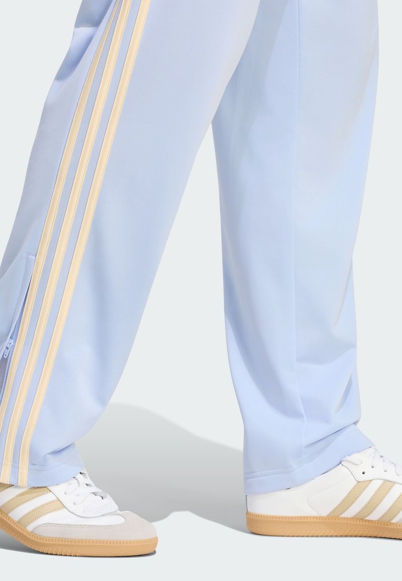 Hellblaue Hosen mit beigen Streifen kombiniert mit weißen Sneakers mit beigen Streifen und Gummisohlen.