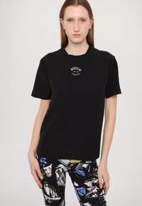 Melnas kokvilnas T-kreklas ar apaļu apkakli, īsām piedurknēm un baltu grafisko logotipu "Moschino Jeans", kas izdots uz krūšu daļas.