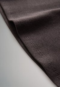 Gros plan sur un tissu côtelé brun foncé avec une couture visible sur un bord plié.