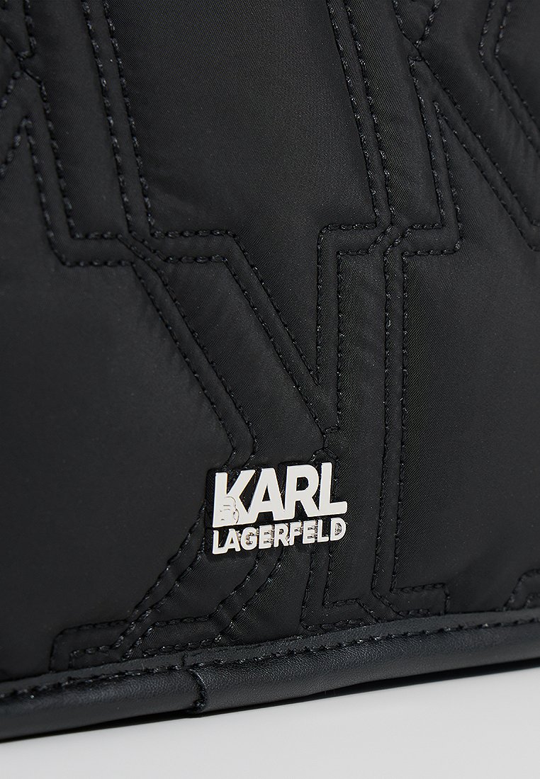 Sac en nylon matelassé noir présentant des coutures géométriques en relief, une plaque logo argentée avec "KARL LAGERFELD" et une texture lisse.