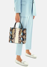 Sac à main carré avec un motif imprimé serpent multicolore dans des tons de brun, bleu et blanc. Doté de poignées noires et d'accents en metal doré.