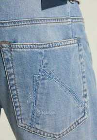 Jeans de mezclilla azul claro con un diseño de costura triangular distintivo en el bolsillo trasero, con costuras en contraste y un acabado texturizado.