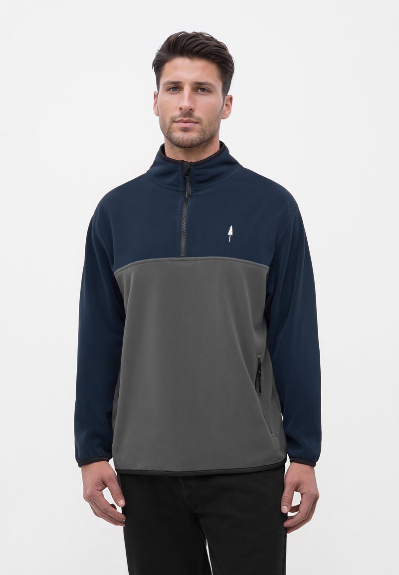 Fleece pullover in marineblauw en grijs. Heeft een half-rits voorkant, hoge kraag en een klein boompje logo op de borst. Zachte textuur.