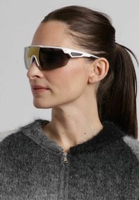 Solsikkers med en slank hvid ramme, mørke linser og kantet design. Båret af en person i en grå sweater, der viser minimale hardwaredetaljer.