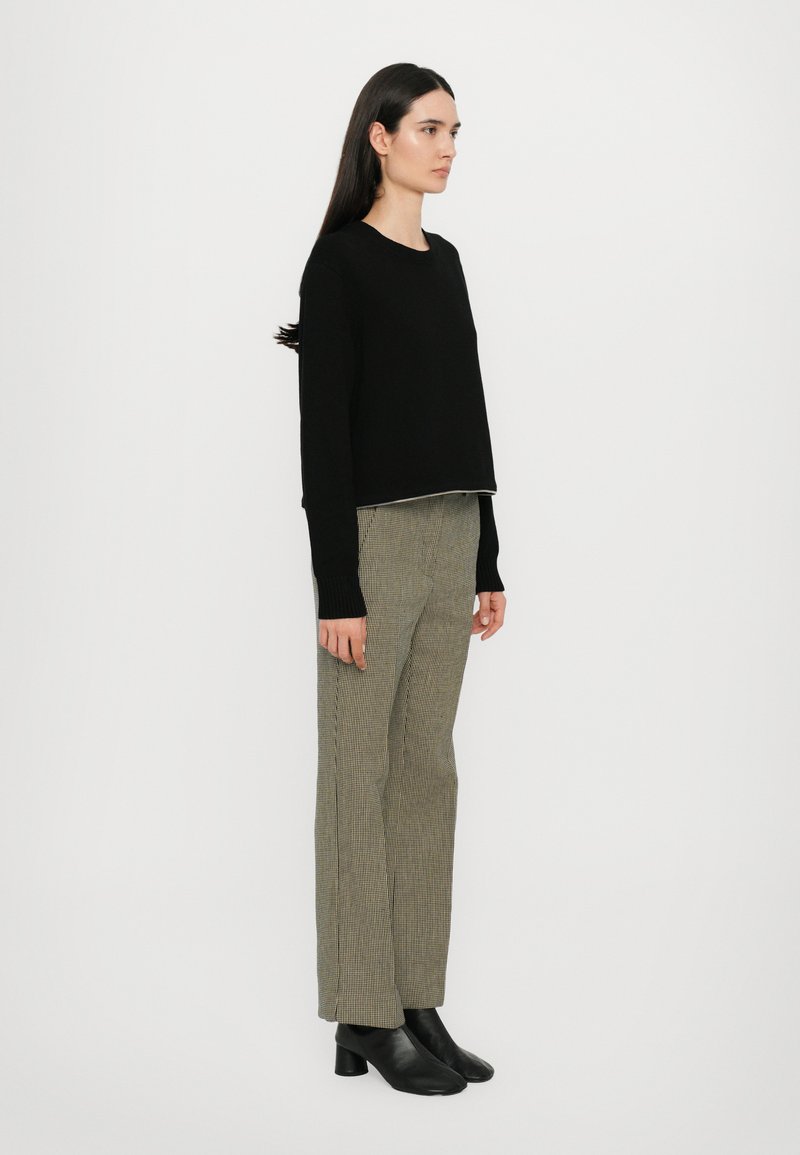 Black cropped sweater, knit texture, paired with checked tapered trousers in green and beige. Black heeled ankle boots complete the outfit.