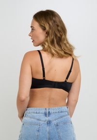 Reggiseno nero con spalline regolabili, una texture liscia e una chiusura a gancio sul retro, abbinato a jeans a vita alta di colore blu chiaro.