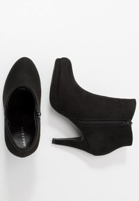 Stivale alla caviglia nero in suede con una texture liscia, dotato di tacco alto, punta a mandorla e cerniera laterale per la chiusura.