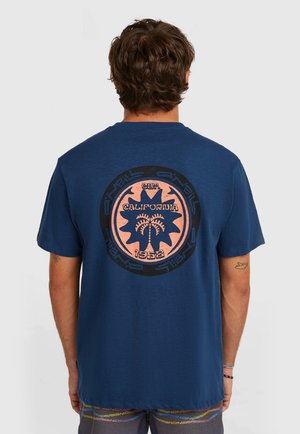 Marineblauw T-shirt van katoen, met een grote cirkelvormige afbeelding op de achterkant in roze en zwart met palmelementen en tekst.