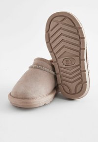 Chaussons en suède beige clair au design simple, à bout rond, à profil bas, et avec une semelle en caoutchouc texturée au motif en zigzag.