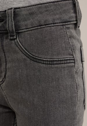 Jeans in denim grigio scuro con una texture liscia, design a cinque tasche e cuciture a contrasto lungo le cuciture. La cintura ha passanti per cintura.