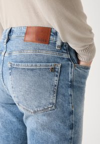 Os jeans de ganga azul claro apresentam um patch de couro castanho rotulado "BOSS", design de cinco bolsos e detalhes de costura distintos.