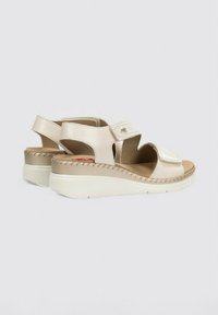 Sandalias de cuña beige con parte superior de cuero, correas de velcro y un borde cosido. Incluyen una plantilla acolchada y una suela de goma texturizada.