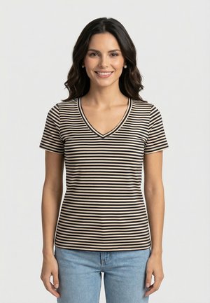 Donna sorridente con capelli scuri che indossa una maglia a righe nere e beige con scollo a V e maniche corte, abbinata a jeans azzurri, su sfondo neutro.