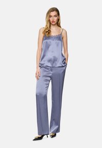 Satin-Camisole in Lavendel mit Spitzendetails, kombiniert mit passenden satinweiten Hosen. Die Absätze haben eine goldene Akzentuierung. Sanfte, elegante Textur.