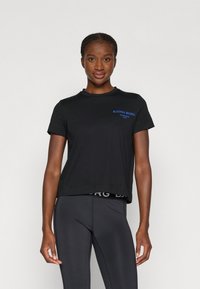 Juodas trumpomis rankovėmis marškinėliai su mėlynu "BJÖRN BORG" logotipu, apvalia kaklo linija ir laisvu siluetu; derinami su juodomis sportinėmis leggingais su logotipo elastine juosta.