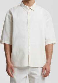 Camicia beige chiaro in lino a maniche corte con colletto e bottoni, caratterizzata da una vestibilità ampia e tessuto testurizzato per una migliore traspirabilità.