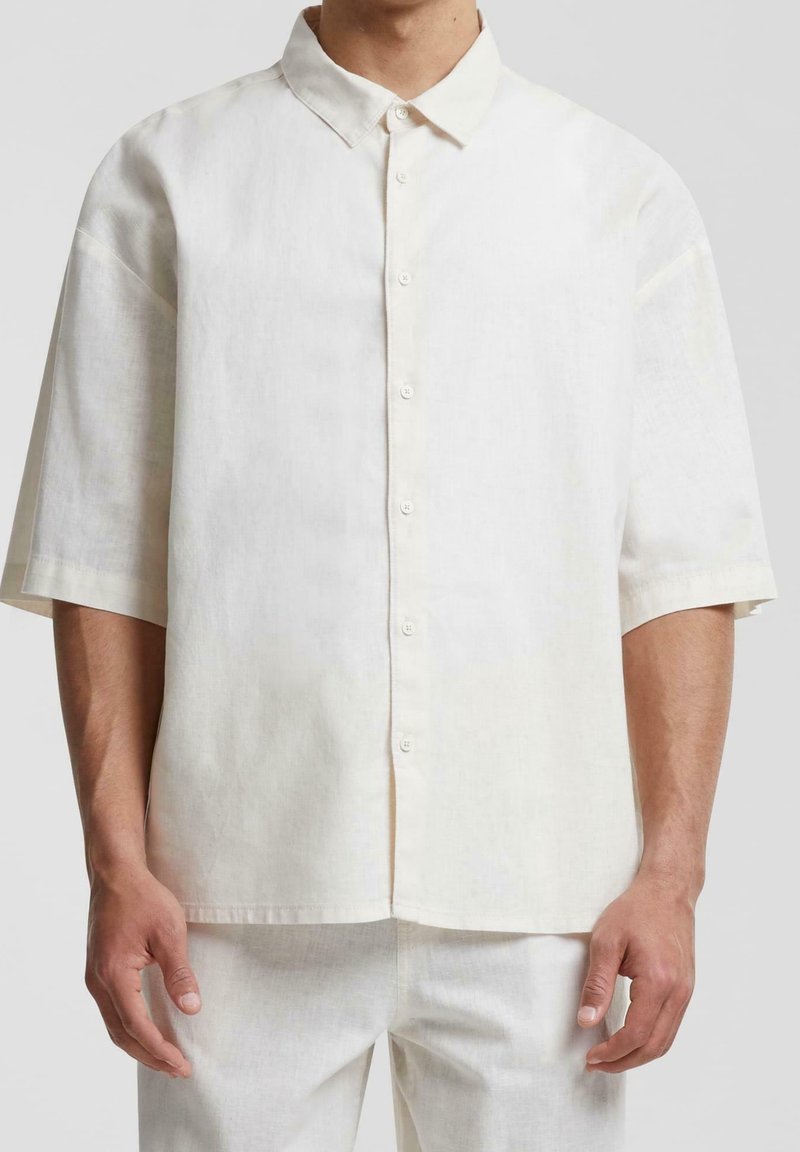 Camicia beige chiaro in lino a maniche corte con colletto e bottoni, caratterizzata da una vestibilità ampia e tessuto testurizzato per una migliore traspirabilità.