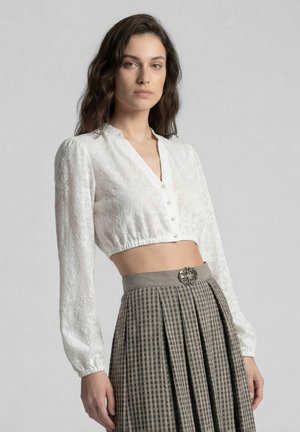 Frau trägt weiße, langärmelige, kurze Bluse mit Blumenmuster und hoch taillierten, plissierten, grau karierten Rock mit dekorativer Gürtelschnalle.