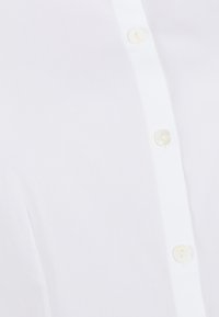 Camisa blanca de botonadura con una textura suave y una fila de botones parecidos a perlas a lo largo de la tapeta, con un diseño nítido y limpio.