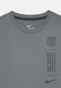 Šedé bavlnené tričko s okrúhlym výstrihom, ktoré má na prednej strane potlačené logo FC Barcelona a text v čiernej farbe, spolu s Nike swoosh.