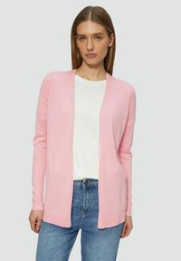 Lichtroze cardigan van zacht materiaal, met lange mouwen, een open voorkant en een gladde textuur. Gecombineerd met een witte t-shirt en jeans.