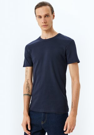 Camiseta de rayas marinas con mangas cortas y cuello redondo, con un diseño ajustado y una textura sutil, combinada con jeans oscuros.
