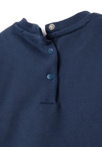 Marineblauwe gebreide top met een geribde ronde hals, voorzien van twee knoopsluitingen aan de voorkant en een gladde textuur, ontworpen met een klein tab-detail.