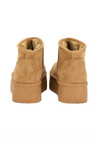 Botas de tobillo de ante color canela con un suave forro de piel y suelas de goma gruesa. Presentan una forma redondeada con una lengüeta en la parte posterior para facilitar su puesta.