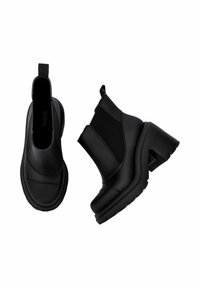 Bottines noires à talon épais, en matériau synthétique lisse avec des panneaux latéraux élastiques pour un enfilage facile. Semelle texturée pour une meilleure adhérence.